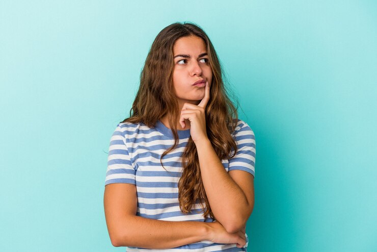 Foto joven mujer caucásica aislada sobre fondo azul mirando hacia los lados con expresión dudosa y escéptica.