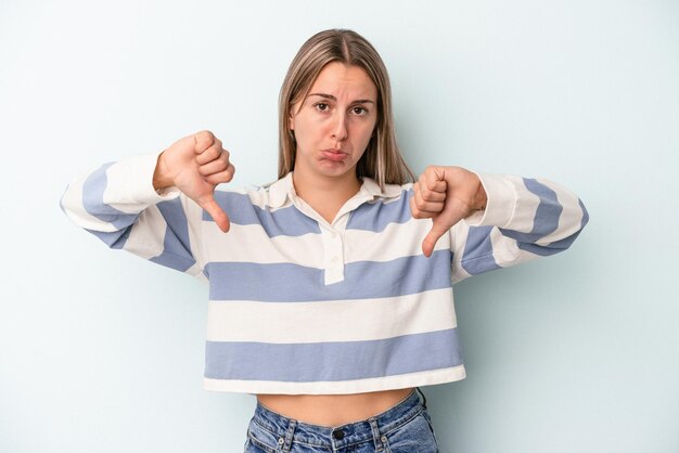 Joven mujer caucásica aislada sobre fondo azul mostrando un gesto de aversión, pulgares hacia abajo. Concepto de desacuerdo.