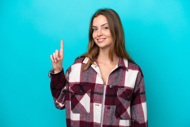 Joven mujer caucásica aislada sobre fondo azul mostrando y levantando un dedo en señal de lo mejor