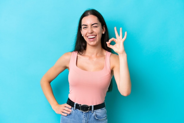 Joven mujer caucásica aislada sobre fondo azul mostrando signo ok con los dedos