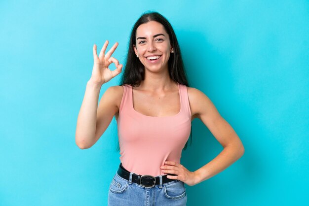 Joven mujer caucásica aislada sobre fondo azul mostrando signo ok con los dedos