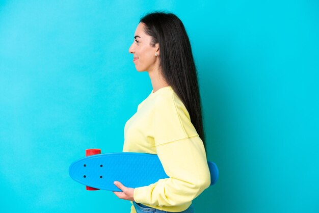 Joven mujer caucásica aislada sobre fondo azul con un patín