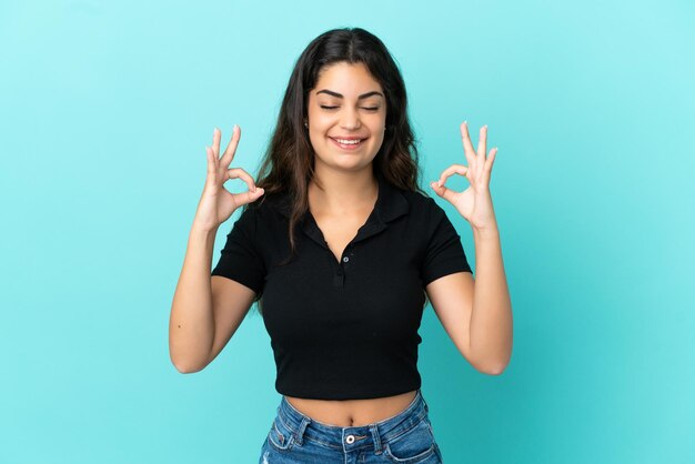 Joven mujer caucásica aislada sobre fondo azul en pose zen