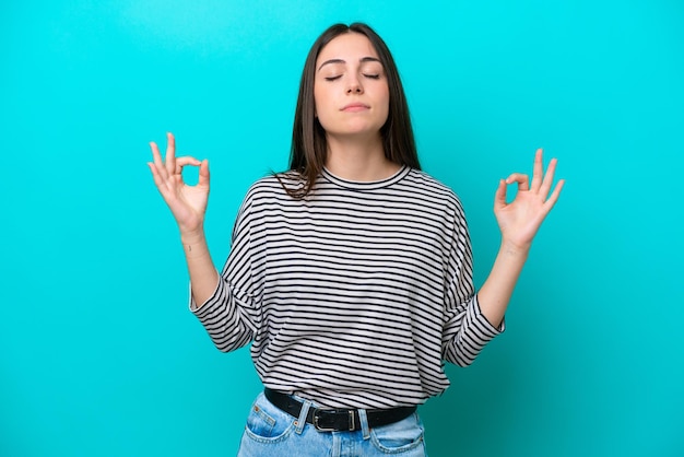 Joven mujer caucásica aislada sobre fondo azul en pose zen