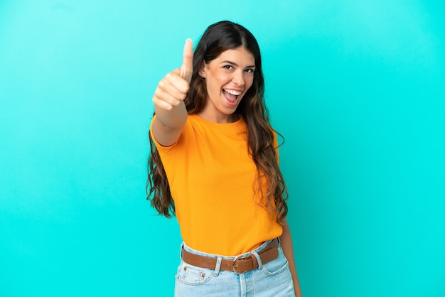 Joven mujer caucásica aislada sobre fondo azul con los pulgares hacia arriba porque ha sucedido algo bueno