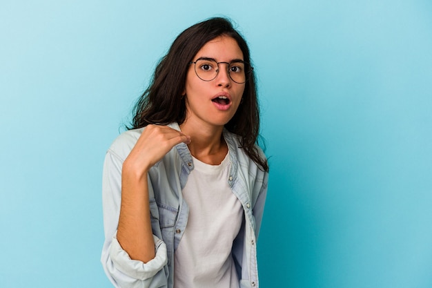 Joven mujer caucásica aislada sobre fondo azul riendo de algo, tapándose la boca con las manos.