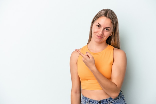 Foto joven mujer caucásica aislada sobre fondo azul sonriendo y apuntando a un lado, mostrando algo en el espacio en blanco.