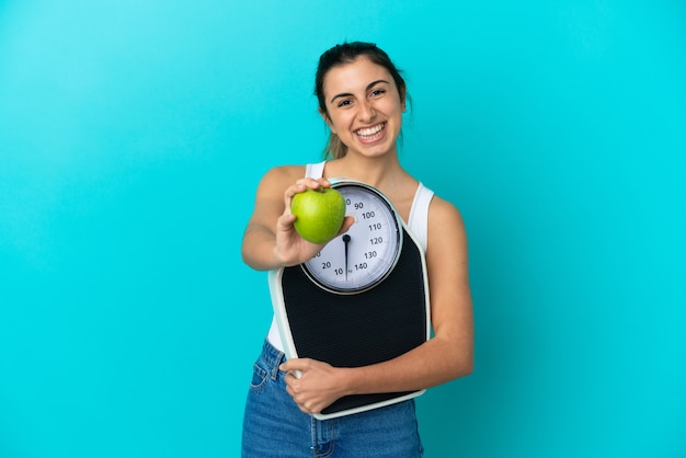 Foto joven mujer caucásica aislada sobre fondo azul sosteniendo una balanza y ofreciendo una manzana