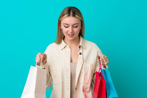 Joven mujer caucásica aislada sobre fondo azul sosteniendo bolsas de la compra y mirando dentro