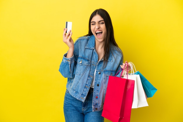 Joven mujer caucásica aislada sobre fondo azul sosteniendo bolsas de la compra y una tarjeta de crédito