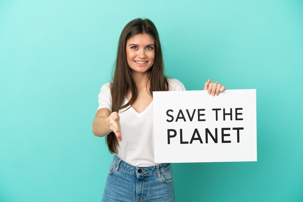 Joven mujer caucásica aislada sobre fondo azul sosteniendo un cartel con texto Save the Planet haciendo un trato