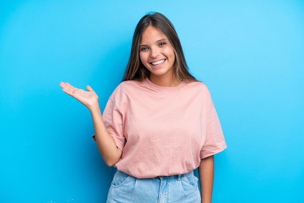 Joven mujer caucásica aislada sobre fondo azul sosteniendo copyspace imaginario en la palma para insertar un anuncio