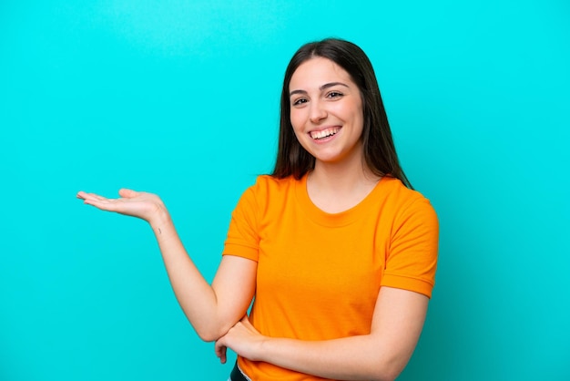 Joven mujer caucásica aislada sobre fondo azul sosteniendo copyspace imaginario en la palma para insertar un anuncio
