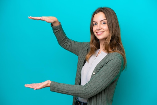 Joven mujer caucásica aislada sobre fondo azul sosteniendo copyspace para insertar un anuncio