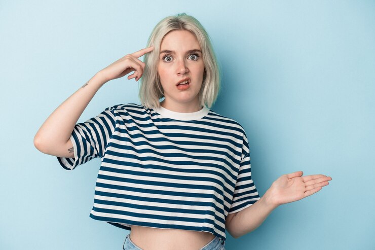 Foto joven mujer caucásica aislada sobre fondo azul sosteniendo y mostrando un producto en la mano.