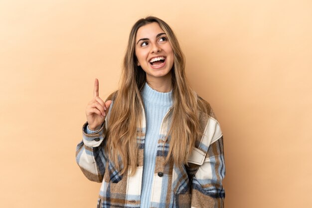 Joven mujer caucásica aislada sobre fondo beige apuntando hacia arriba y sorprendido