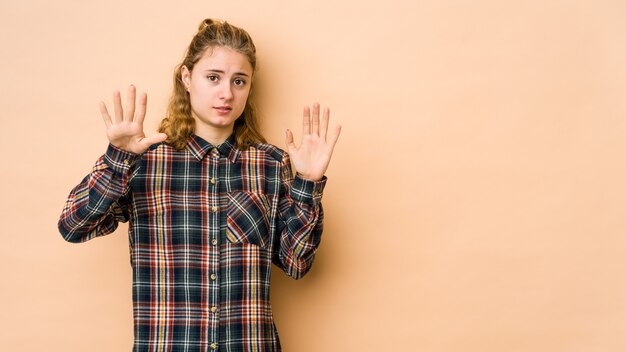 Joven mujer caucásica aislada sobre fondo beige conmocionada debido a un peligro inminente