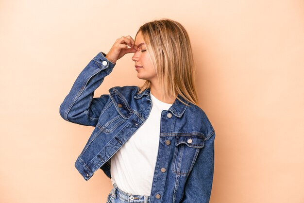 Joven mujer caucásica aislada sobre fondo beige con dolor de cabeza, tocando la parte delantera de la cara.