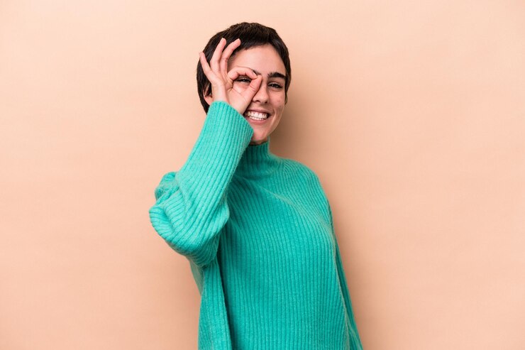 Foto joven mujer caucásica aislada sobre fondo beige emocionado manteniendo el gesto ok en el ojo.