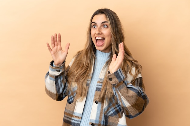 Joven mujer caucásica aislada sobre fondo beige con expresión facial sorpresa