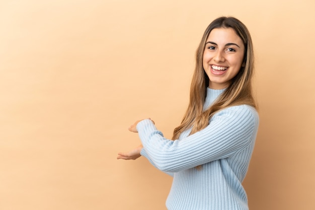 Joven mujer caucásica aislada sobre fondo beige extendiendo las manos