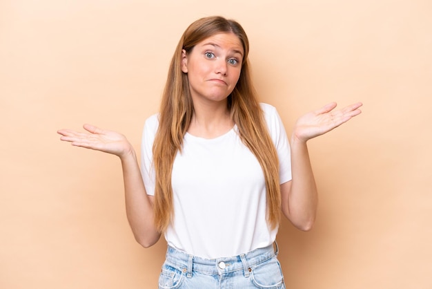 Joven mujer caucásica aislada sobre fondo beige haciendo gesto de dudas