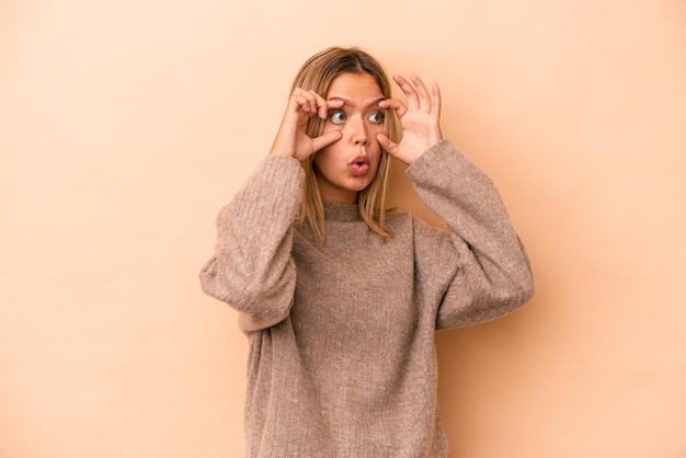 Joven mujer caucásica aislada sobre fondo beige manteniendo los ojos abiertos para encontrar una oportunidad de éxito.