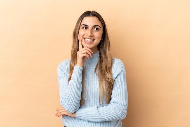 Joven mujer caucásica aislada sobre fondo beige pensando en una idea mientras mira hacia arriba