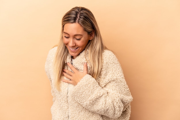 Joven mujer caucásica aislada sobre fondo beige riendo manteniendo las manos en el corazón, concepto de felicidad.