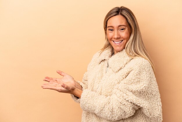 Joven mujer caucásica aislada sobre fondo beige sosteniendo un espacio de copia en una palma.