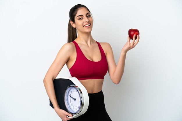 Joven mujer caucásica aislada sobre fondo blanco con báscula y con una manzana