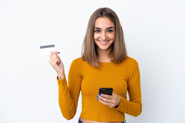 Joven mujer caucásica aislada sobre fondo blanco comprando con el móvil con tarjeta de crédito