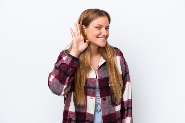 Foto joven mujer caucásica aislada sobre fondo blanco escuchando algo poniendo la mano en la oreja