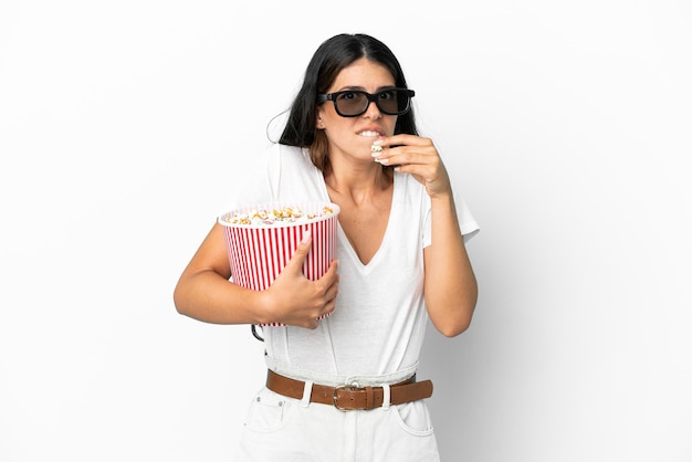 Joven mujer caucásica aislada sobre fondo blanco con gafas 3d y sosteniendo un gran balde de palomitas de maíz