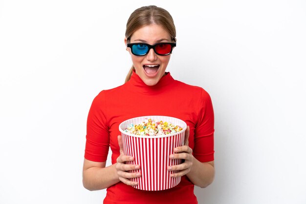 Joven mujer caucásica aislada sobre fondo blanco con gafas 3d y sosteniendo un gran balde de palomitas de maíz