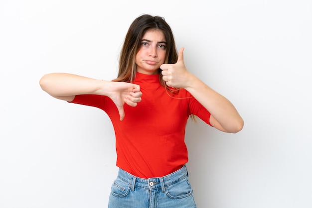 Joven mujer caucásica aislada sobre fondo blanco haciendo buena mala señal indecisa entre sí o no