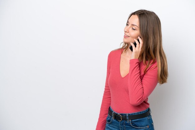 Joven mujer caucásica aislada sobre fondo blanco manteniendo una conversación con el teléfono móvil con alguien