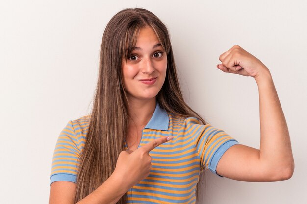 Joven mujer caucásica aislada sobre fondo blanco mostrando gesto de fuerza con los brazos, símbolo del poder femenino