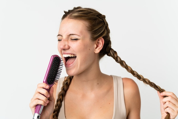 Joven mujer caucásica aislada sobre fondo blanco con peine y cantando