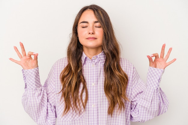 Joven mujer caucásica aislada sobre fondo blanco se relaja después de un duro día de trabajo, ella está realizando yoga.