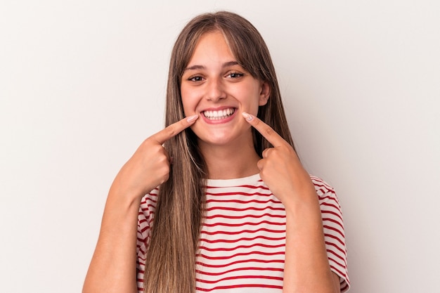 Joven mujer caucásica aislada sobre fondo blanco sonríe, señalando con el dedo a la boca.