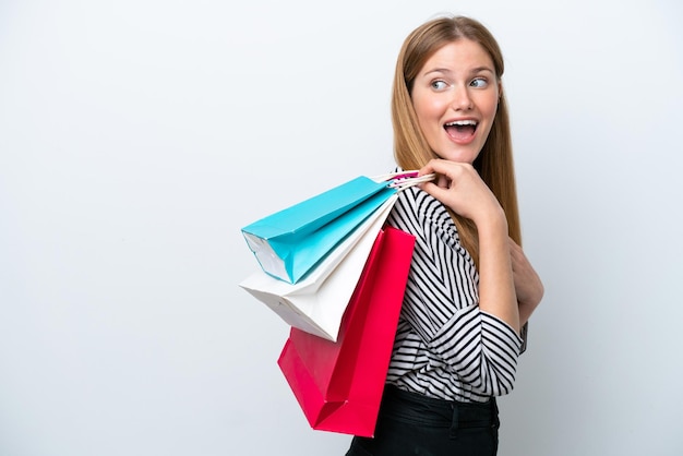 Joven mujer caucásica aislada sobre fondo blanco sosteniendo bolsas de la compra y sonriendo