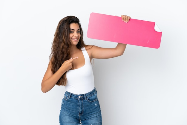 Joven mujer caucásica aislada sobre fondo blanco sosteniendo un cartel vacío y apuntando