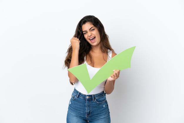 Foto joven mujer caucásica aislada sobre fondo blanco sosteniendo un icono de verificación y celebrando una victoria