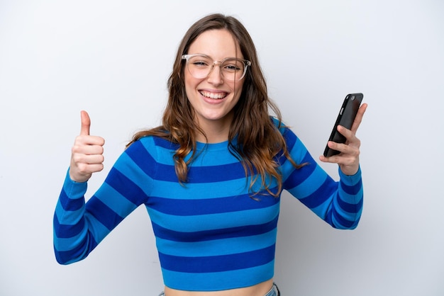 Foto joven mujer caucásica aislada sobre fondo blanco con teléfono móvil mientras hace los pulgares para arriba