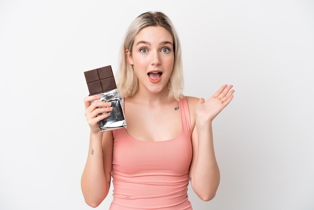 Joven mujer caucásica aislada sobre fondo blanco tomando una tableta de chocolate y sorprendido