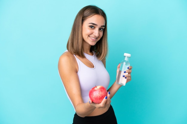 Joven mujer caucásica aislada sobre fondo morado con una manzana y con una botella de agua