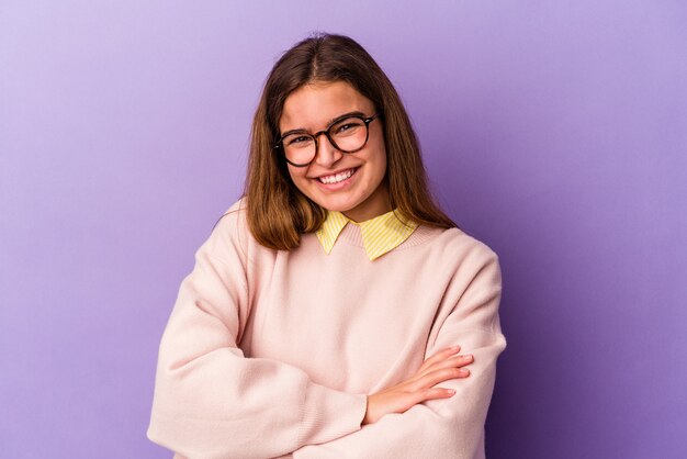 Joven mujer caucásica aislada sobre fondo morado que se siente confiada, cruzando los brazos con determinación.