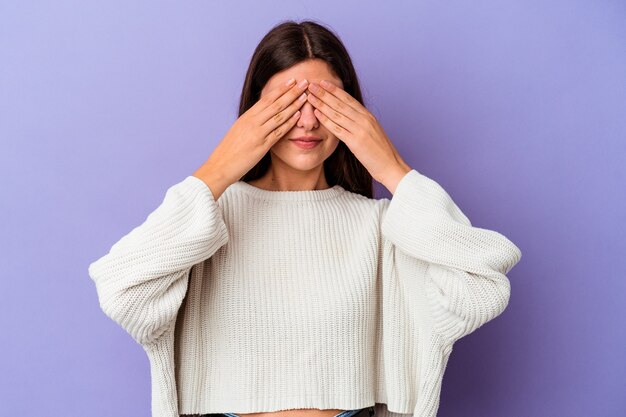 Joven mujer caucásica aislada sobre fondo púrpura miedo cubrirse los ojos con las manos.