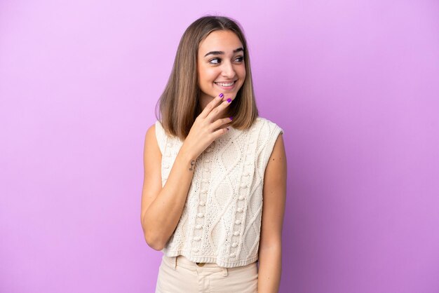 Joven mujer caucásica aislada sobre fondo púrpura mirando hacia arriba mientras sonríe